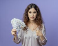 looking-camera-young-pretty-girl-holding-points-cash-isolated-blue-background