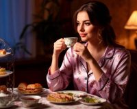 Молодая женщина в красивой пижаме пьет вечером чай с пирожными