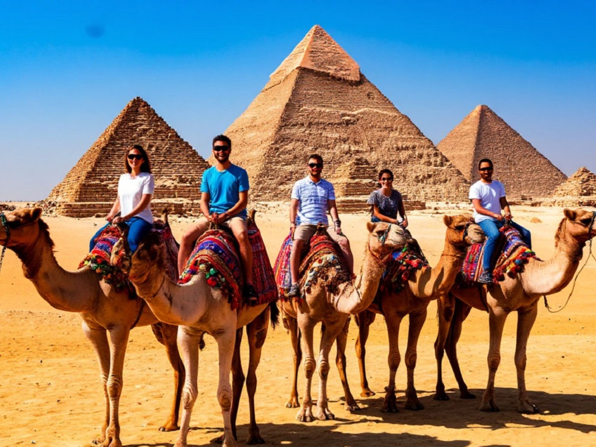 Туристы катаются на верблюдах рядом с египетскими пирамидами